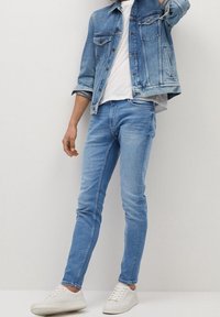Chaqueta de mezclilla azul claro y jeans skinny a juego, combinados con una camiseta blanca y zapatillas blancas. Tejido suave con características de diseño clásico.