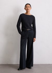 Μαύρο πλεκτό πουλόβερ με βαθούλωτο λαιμό, συνδυασμένο με ψηλοκάβαλο μαύρο παντελόνι wide-leg και μια λεπτή μαύρη ζώνη με χρυσό αγκράφα.