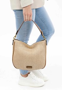 Sac hobo en paille tissée avec une texture lisse, de couleur beige, associé à une bandoulière en cuir et un accent en laiton doré.