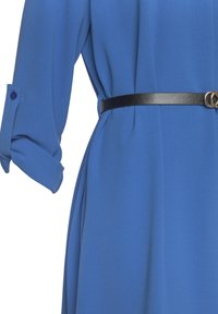 Modrá blůza vyrobená z lehkého materiálu, s dlouhými rukávy a detaily na knoflíky, a černým koženým páskem se zlatou sponou ve tvaru kruhu.