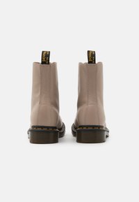 Botas de tobillo de cuero beige con costuras amarillas y suelas de goma negras, que cuentan con tiradores en la parte trasera para facilitar su puesta.