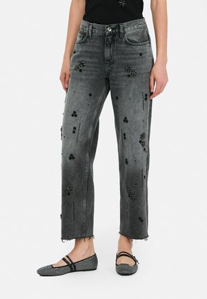 Zwarte denim jeans met een verweerd uiterlijk en gestructureerde zwarte versieringen, gecombineerd met lage zwarte platte schoenen met rhinestone-accenten.
