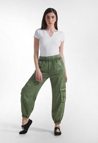 Hvid kortærmet top med V-hals og grønne cargo-bukser med elastik i taljen, sidelommer og opsmøgede ben, stylet med sorte flade sko.
