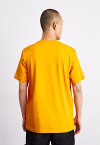 T-shirt arancione a maniche corte in cotone con collo a giro, texture liscia e vestibilità rilassata; presenta nessun motivo o accento evidente.