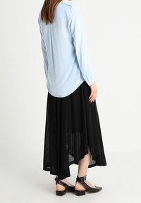 Blusa a maniche lunghe azzurro chiaro con orlo arrotondato e dettagli con bottoni, abbinata a una gonna nera fluida e asimmetrica e sandali neri con cinturino.