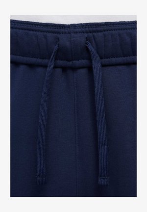 Tummansiniset collegehousut, joissa on nyöri vyötäröllä, pehmeä tekstuuri, joustavat hihnat ja tasainen kangas, jossa on minimaalista saumayksityiskohtaa.