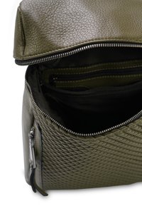 Olijfgroene tas van textuurmateriaal met een ritssluiting. Inclusief binnenvakken en een zijvak met ritssluiting voor organisatie.