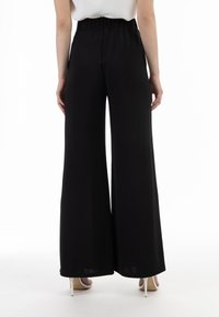 Schwarze weit geschnittene Hose mit hohem elastischen Bund. Glatter, leichter Stoff fällt elegant. Hat einen sauberen Saum am unteren Ende.