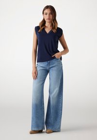Marinblus, t-shirt med kort ärm och V-ringning; matchad med ljusblå, vida jeans med en urblekt textur och klassisk femfickdesign.
