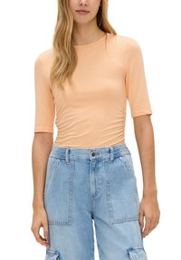 Pfirsichfarbendes, enganliegendes T-Shirt mit kurzen Ärmeln und gerafften Details an den Seiten, kombiniert mit hellblauen Cargo-Jeans mit mehreren Taschen.