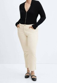 Maglietta nera a costine con maniche lunghe e chiusura a bottoni, abbinata a pantaloni dritti color crema e scarpe nere con dettagli borchiati.