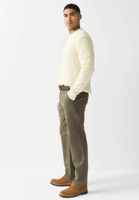 Kreemikas värvi kootud särk, oliivrohelised püksid ja pruunid seemisnahast kingad, särgil on tekstuuriline muster ja pruun vöö.