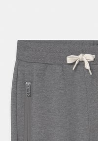 Gray sweatpants feature a drawstring waistband with a cream tie and a zippered pocket on the side. Material is soft and textured.