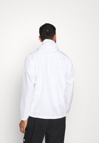 Chaqueta blanca ligera con un alto cuello, detalles de costura y puños elásticos. Diseñada para uso al aire libre, cuenta con bolsillos laterales.