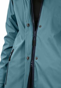 Teal waterproof jacket featuring a navy zipper, snap buttons, and a side pocket. Smooth texture with a fitted design for functionality.
