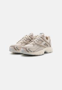 Beige mesh sneakers with layered overlays, textured details, and a cushioned sole. Features white laces and subtle branding on the tongue.