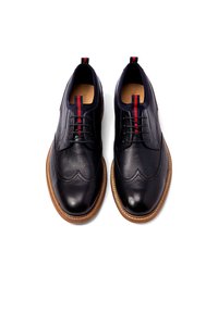 Marine leren schoenen met een gladde textuur, wingtip-details, contrasterende rode en marine blauwe strepen, en een tan rubberen zool.