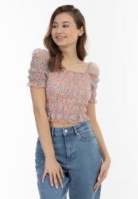 Top corto all'uncinetto con maniche a sbuffo, motivo floreale multicolore, corpino elasticizzato, orlo arricciato, abbinato a jeans a vita alta di colore azzurro chiaro.