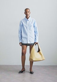 Heledad sinine triibuline särk, teksaseelik, mustad lamedad kingad, hoides käes beeži kotti, millel on tekst "THE BACK BAG". Puhtad jooned, juhuslik disain, modernne välimus.
