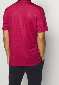 Polo tričko s krátkým rukávem v jasně růžové barvě s texturovaným vzorem. Černý límeček a postranní rozparky pro pohodlí. Vyrobeno z prodyšného materiálu.