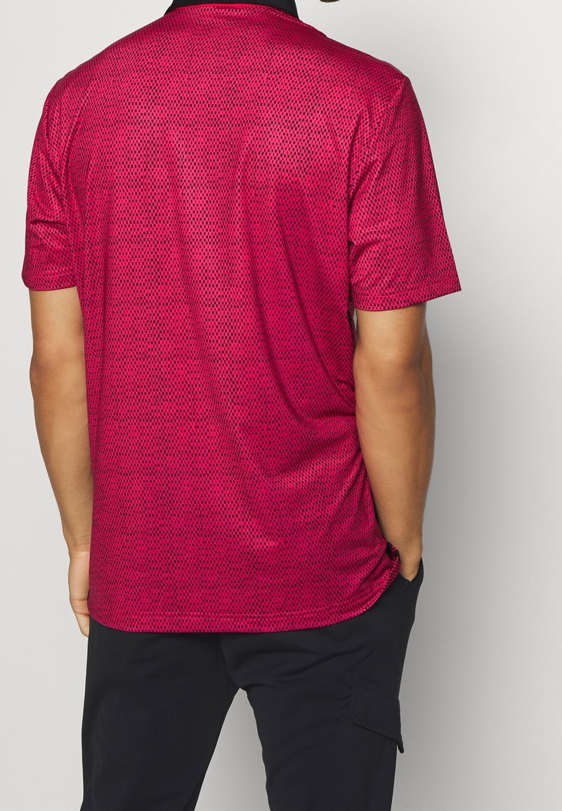 Polo tričko s krátkým rukávem v jasně růžové barvě s texturovaným vzorem. Černý límeček a postranní rozparky pro pohodlí. Vyrobeno z prodyšného materiálu.