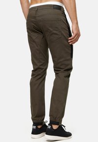 Pantalones cargo verde oliva con un ajuste slim, puños elásticos, paneles laterales negros y múltiples bolsillos traseros. Llevados con zapatillas negras.
