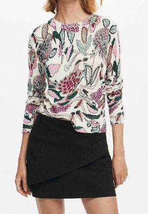 Weißes Langarmshirt mit pink-grünem Blumenmuster kombiniert mit einem schwarzen asymmetrischen Minirock an einer stehenden Person.