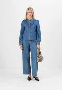 Denim jacket with ruffled collar, light blue color, button-down front; paired with wide-leg denim pants and a snakeskin-patterned handbag.