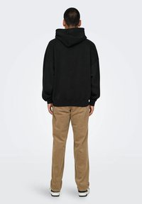 Black hooded sweatshirt with oversized fit, ribbed cuffs and hem. Paired with light brown corduroy pants and black and white sneakers.