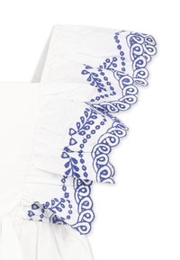 Tessuto di cotone bianco con motivi floreali e spirali ricamati in blu su una manica a balze. Presenta delle pieghe vicino alla spalla.