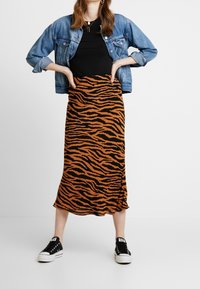 Sukně s tygřím vzorem v oranžové a černé barvě, vyrobená z měkké látky, v kombinaci s černým topem a džínovou bundou, doplněná černými teniskami.