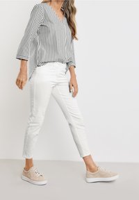 Blusa a rayas en blanco y negro con escote en V, combinada con jeans blancos ajustados y zapatillas beige con una parte superior texturizada y suela blanca.