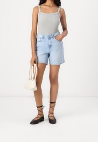 Shorts de mezclilla de color azul claro con una cintura alta y bolsillos. Top de tirantes ajustado gris. Bailarinas negras con lazos en los tobillos. Pequeño bolso blanco sostenido en la mano.