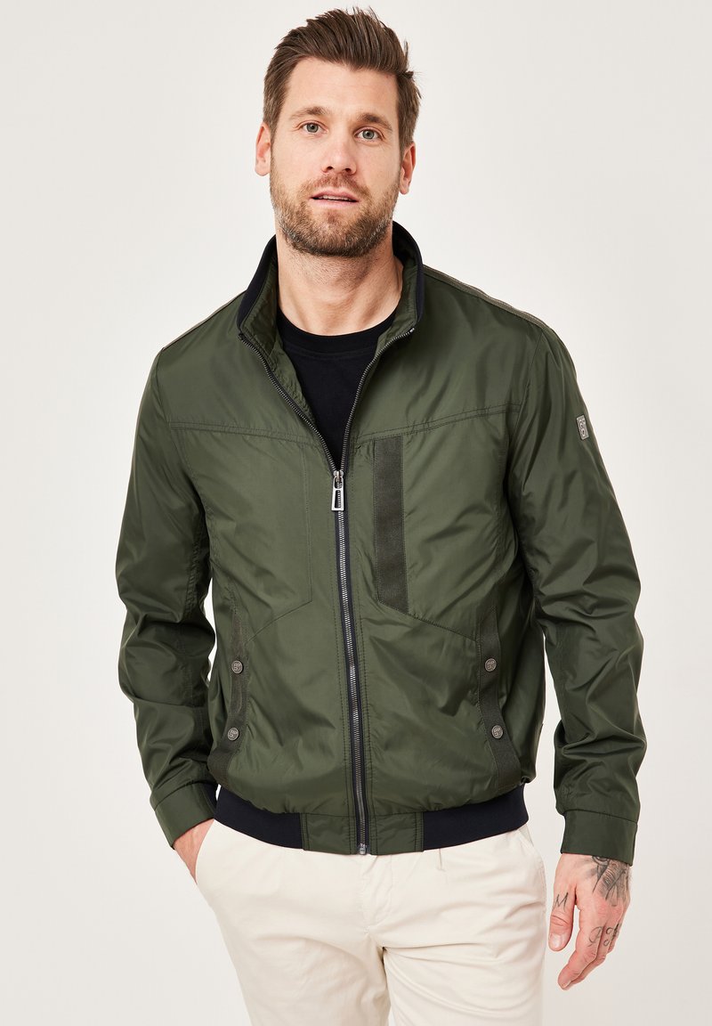 Olivgrüne Bomberjacke mit Reißverschluss vorne, gerippten Bündchen und seitlichen Knöpfen. Verfügt über strukturiertes Material auf der Brust und den Schultern.