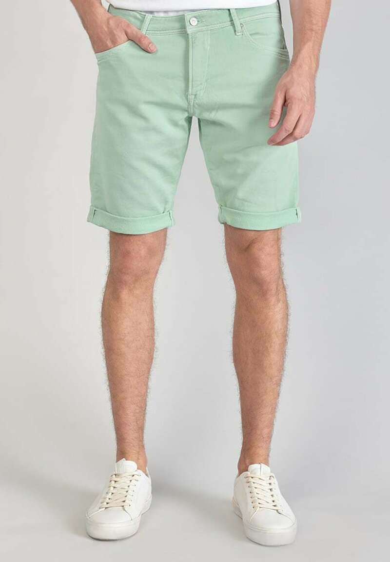 Shorts en coton vert menthe avec des ourlets roulés, dotés de poches latérales et d'une fermeture à bouton à l'avant, associés à des baskets blanches.