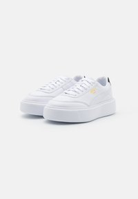 Białe trampki na platformie z gładkiej skóry, okrągłym noskiem, sznurowanym przodem, teksturowaną gumową podeszwą oraz małym czarno-złotym akcentem logo.