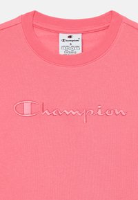 Sweatshirt rosa com decote redondo, apresentando um logótipo "Champion" bordado na mesma tonalidade. Feito de um tecido de jersey macio.