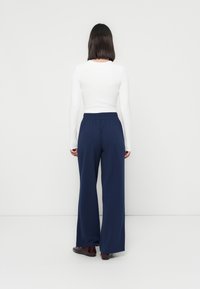 Strakke witte langemouwen top met een ronde hals, gecombineerd met lichte, marineblauwe wijde broek met een elastische tailleband.
