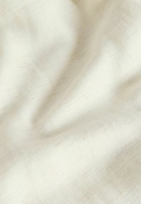 Material moale de culoare crem, cu țesătură subtilă în model coadă de pește diagonal și pliuri ușoare ce creează umbre delicate.
