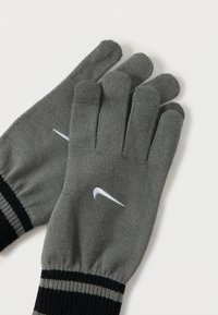 Sive pletene rukavice s crnim i sivim prugastim manžetama i bijelim logotipom u obliku swoosh na stražnjoj strani svake ruke, položene ravno na bijelu površinu.