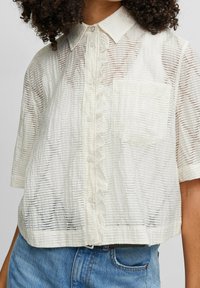 Vit skjorta med knapp-up, volang i placket, korta ärmar och en strukturerad randig mönster. Har en bröstficka och kort design.