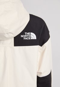 Bijela i crna jakna s kapuljačom, s logotipom The North Face u bijeloj boji na crnom dijelu, glatke teksture i dizajna u više boja.
