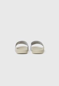 Bageste udsigt af to slidesandaler med en beige ydersål og lysegrå overdel i blødt meshmateriale og åbent tådesign.