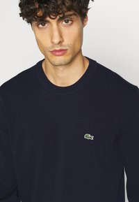 Navy blue sweater made of knit fabric featuring a round neckline and a small green crocodile logo on the left chest.