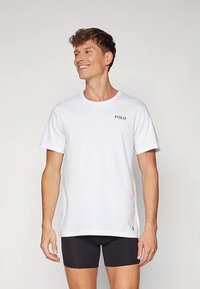 Λευκό βαμβακερό μπλουζάκι με στρογγυλή λαιμόκοψη και κοντά μανίκια, με μικρό μαύρο λογότυπο "POLO" στο αριστερό στήθος. Φορεμένο με μαύρες βερμούδες.