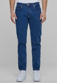 Traperice tamnoplave boje sa slim fit krojem, s kopčanjem na dugme, dizajnom s pet džepova i minimalističkim šivanjima. Uparene s bijelim tenisicama.