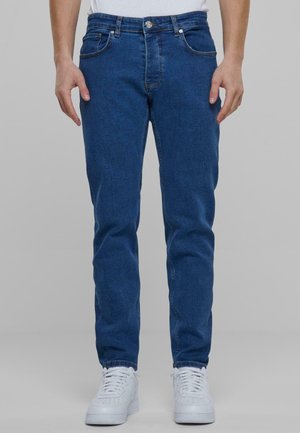 Tummansinisiä farkkuja slim fit -mallilla, jossa on napitus, viiden taskun muotoilu ja minimalistinen saumaus. Yhdistettynä valkoisiin lenkkarit.