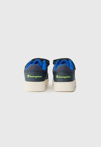 Zapatillas deportivas en azul y negro con un upper texturizado, suela blanca y logotipo verde de Champion en el talón. Cuentan con tiras de Velcro para el cierre.