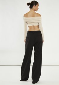 Top beige scollato con texture arricciata, abbinato a pantaloni neri a vita alta e gamba larga. Tessuti lisci con una silhouette aderente.