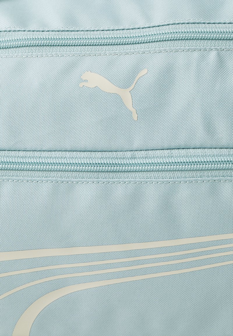 Borsa di stoffa azzurra con due tasche con zip, caratterizzata da un logo Puma bianco e da design a linee curve eleganti in una tonalità più chiara.